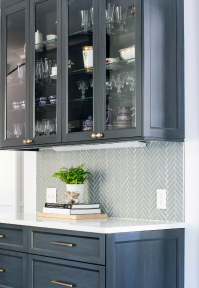 Kitchen counter with dark blue glass-faced cabinets and subtle green herringbone backsplash
