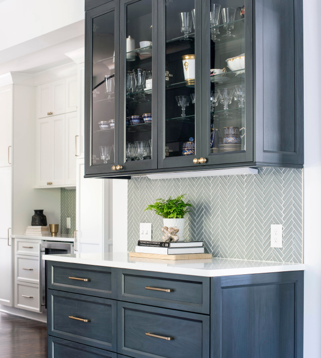 Kitchen counter with dark blue glass-faced cabinets and subtle green herringbone backsplash