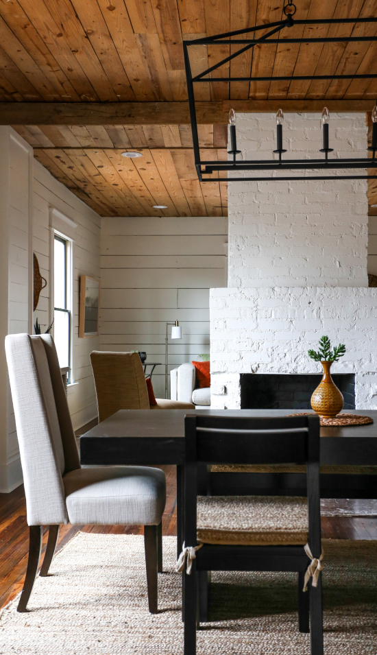 Cozy modern dining area with double-sided white fireplace and rustic wood-paneled ceiling