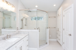 Remodeled primary bath with white countertops and vanity, white tile floor, glass-enclosed shower, and recessed lighting.